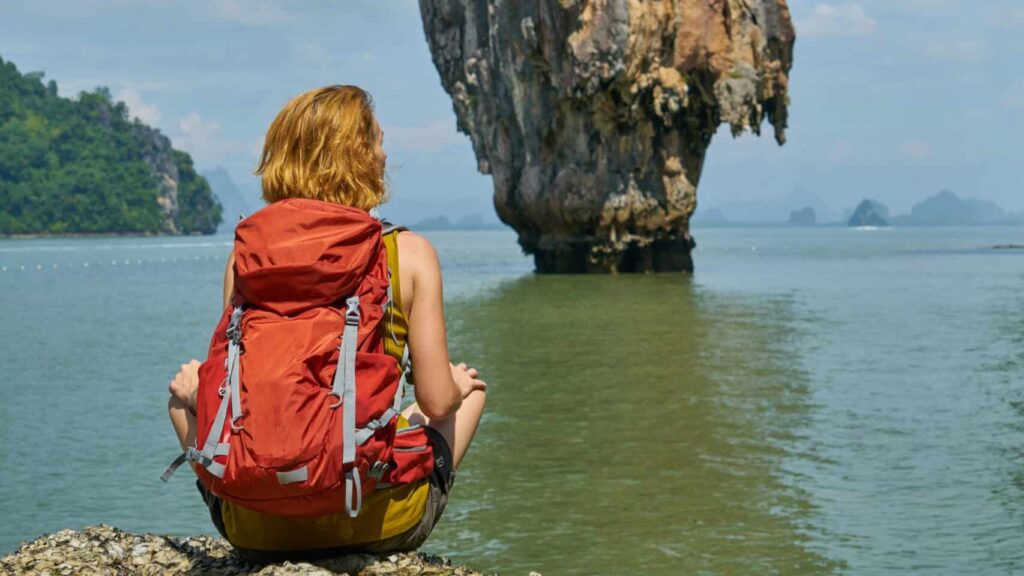 woman in red dress sitting on rock formation near body of water during daytime