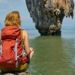 woman in red dress sitting on rock formation near body of water during daytime