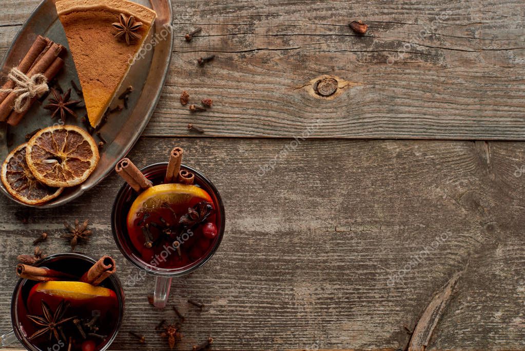 top view of piece of pie and red spiced mulled wine with berries, anise, orange slices and cinnamon on wooden rustic table