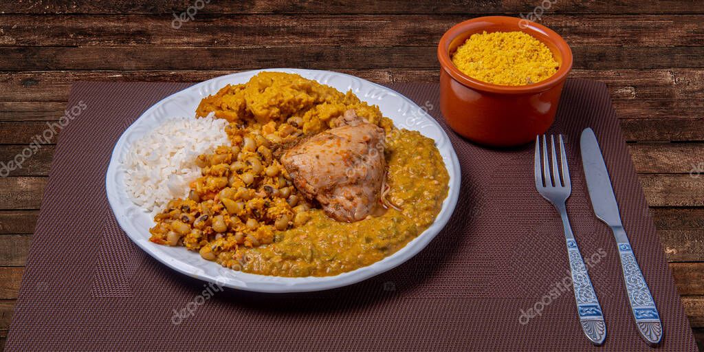 Traditional Afro Brazilian dish made with okra and dried shrimp accompanied by vatap, beans, rice, chicken and manioc flour on a wooden table.